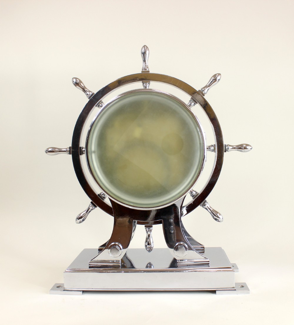 A chrome-plated nautical desk clock styled as a ship wheel mounted on a rectangular plinth with a cream dial and Roman numerals. View V
