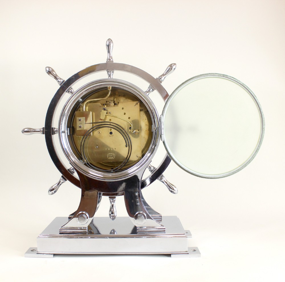 A chrome-plated nautical desk clock styled as a ship wheel mounted on a rectangular plinth with a cream dial and Roman numerals. View VI