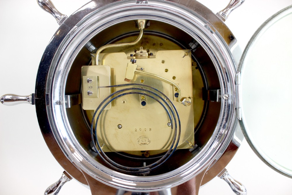 A chrome-plated nautical desk clock styled as a ship wheel mounted on a rectangular plinth with a cream dial and Roman numerals. View VIII