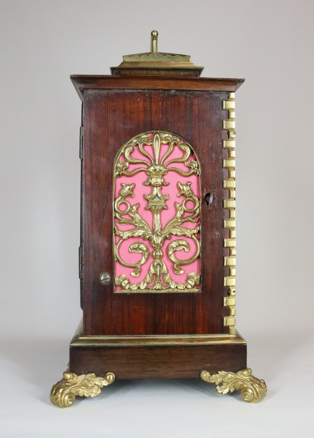 A mahogany and brass bracket clock featuring a white enamel dial with Roman numerals, gilt brass corner mounts, and scroll feet. View X