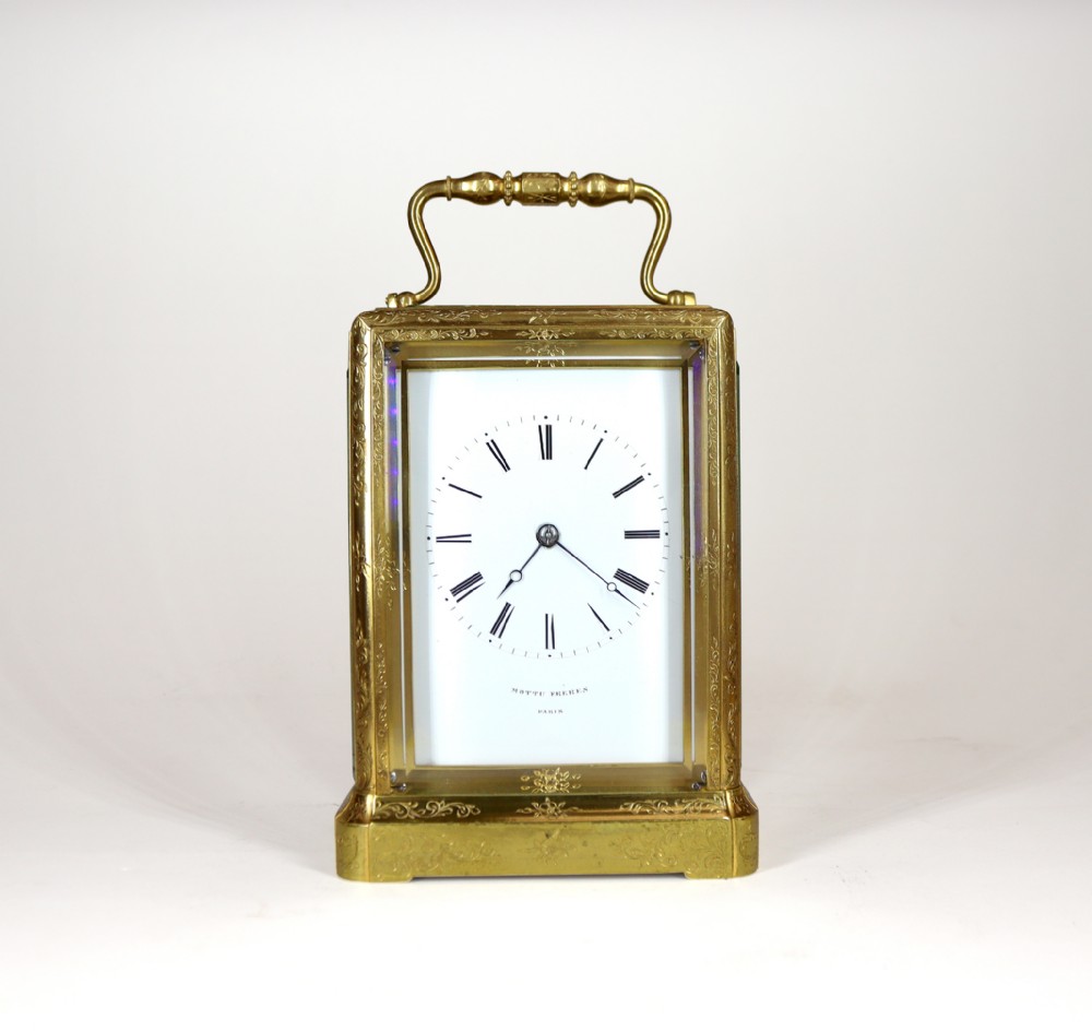 An engraved gilt brass carriage clock with a top carrying handle, glass side panels, and a white enamel dial displaying Roman numerals.