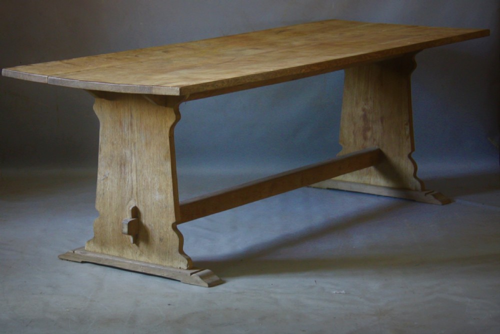 A rectangular bleached oak refectory dining table featuring shaped trestle end supports connected by a pegged central stretcher. View II