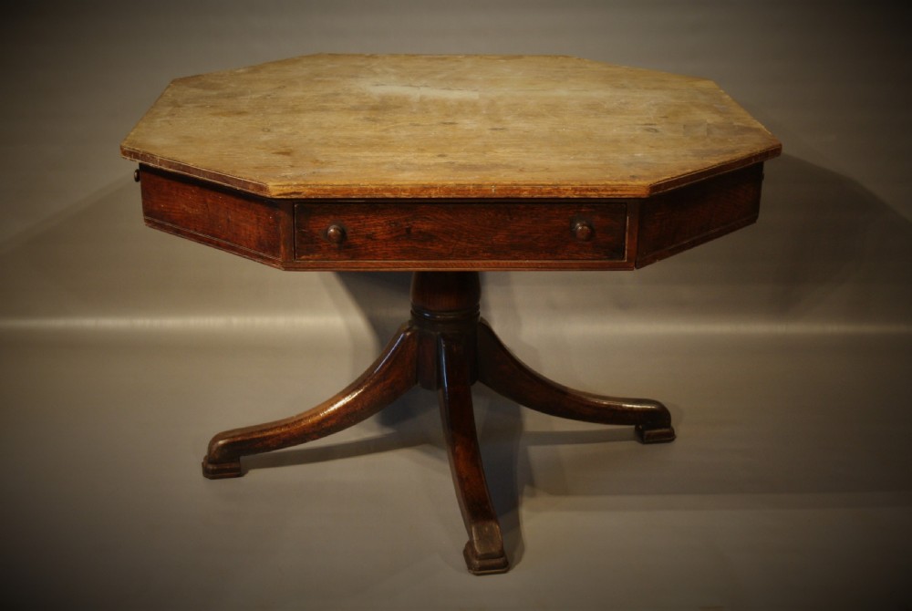An antique Victorian octagonal oak drum table featuring frieze drawers with turned wooden knobs, supported by a central turned pedestal with four splayed legs.