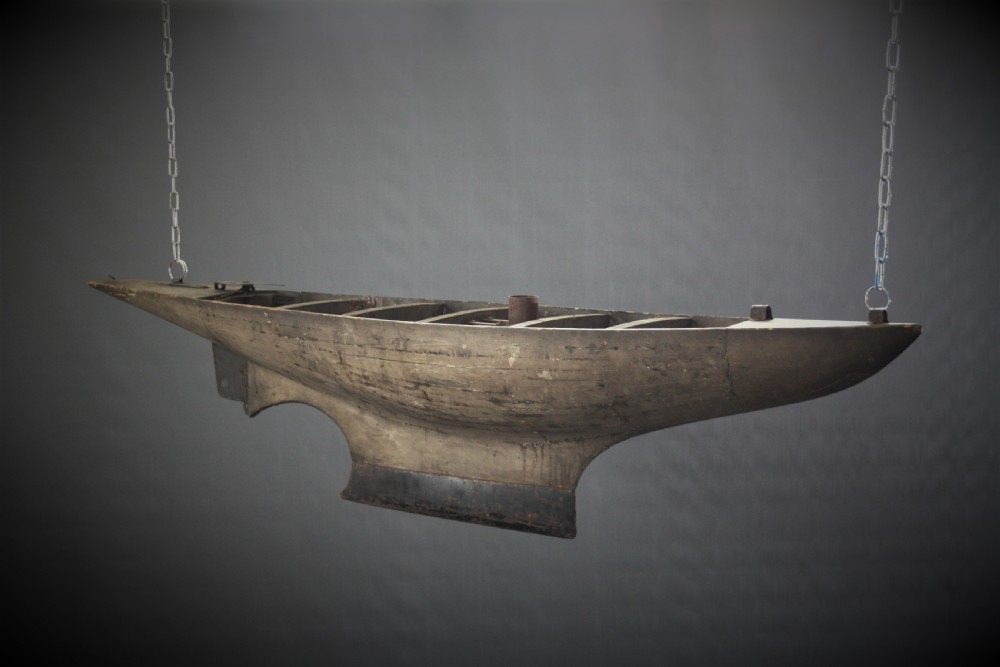 A large carved wooden pond yacht hull featuring exposed interior deck ribs and a weighted metal keel.