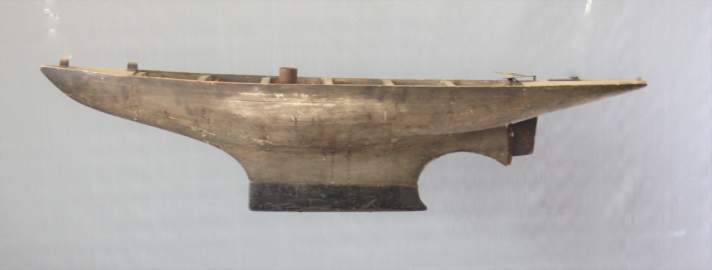 A large carved wooden pond yacht hull featuring exposed interior deck ribs and a weighted metal keel. View III