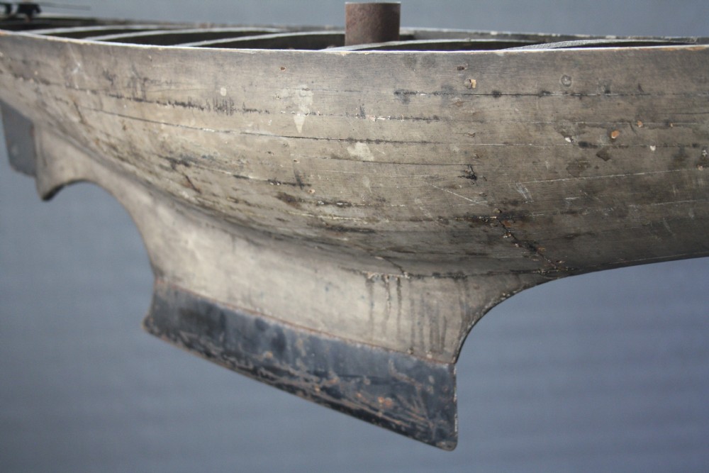 A large carved wooden pond yacht hull featuring exposed interior deck ribs and a weighted metal keel. View V