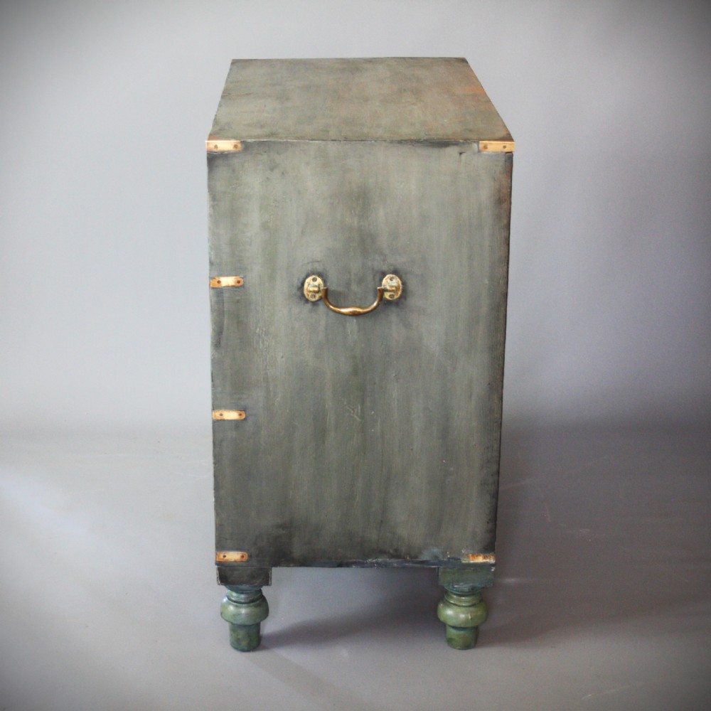 A Victorian green painted campaign chest of drawers with flush brass corner mountings, recessed brass handles, side carrying handles, and turned feet. View II