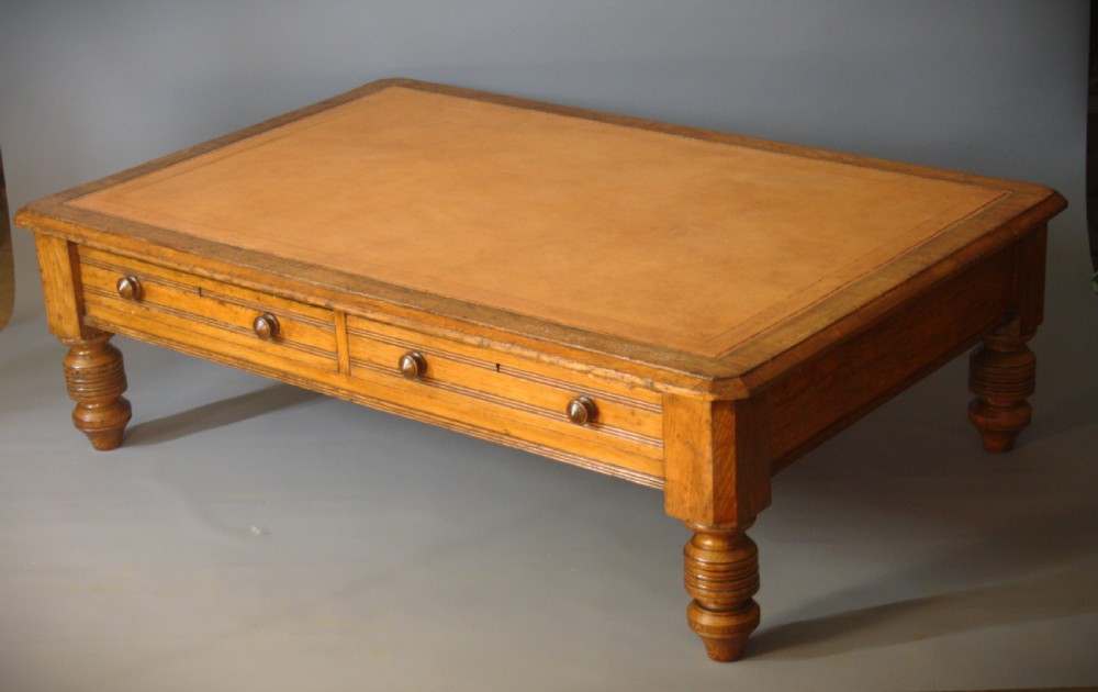 A low rectangular golden oak coffee table featuring a leather inset top, two front drawers with turned wooden knobs, and stout turned legs.