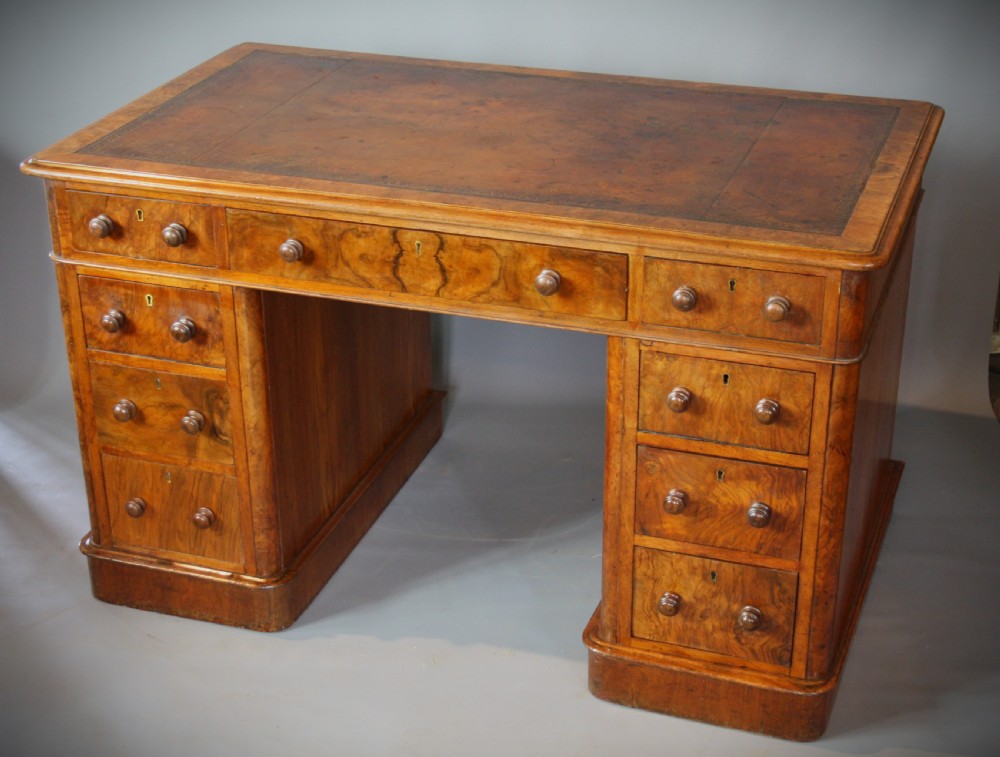 An antique Victorian walnut pedestal desk featuring nine drawers with turned wooden knobs and a leather inset writing surface.