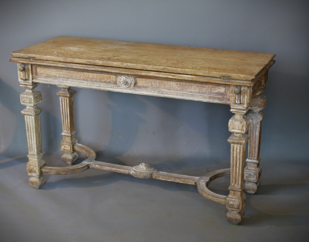An antique light oak metamorphic console table featuring fluted square legs, a central carved rosette on the apron, a curved stretcher, and a hinged fold-over top.