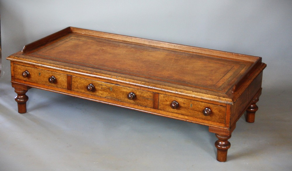 A low rectangular mahogany coffee table featuring an inset brown leather top, raised gallery border, three frieze drawers with turned wooden knobs, and short turned legs.