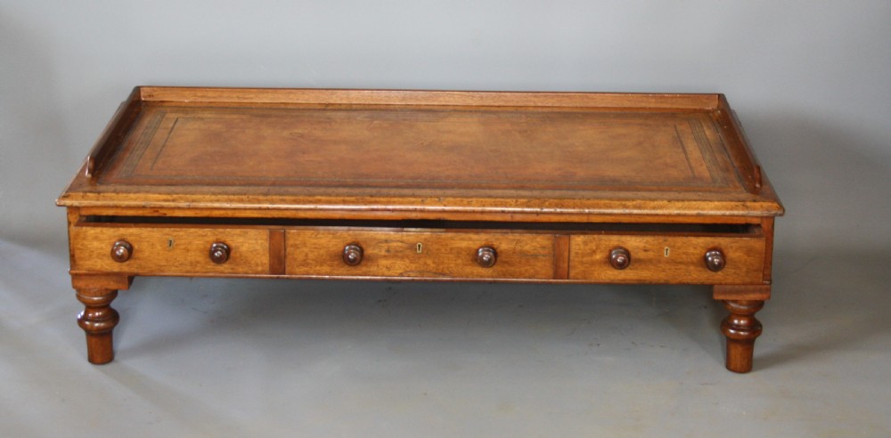 A low rectangular mahogany coffee table featuring an inset brown leather top, raised gallery border, three frieze drawers with turned wooden knobs, and short turned legs. View II