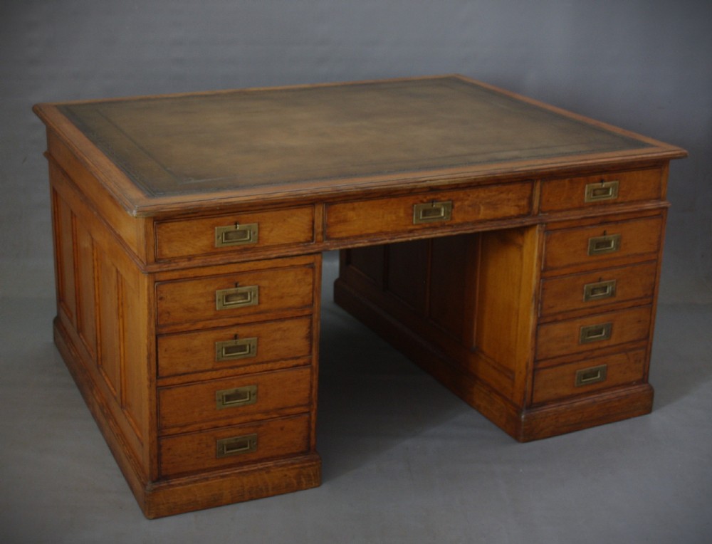 A large Victorian oak partners desk featuring a brown leather inset writing surface, nine front drawers with brass handles, and panelled sides.