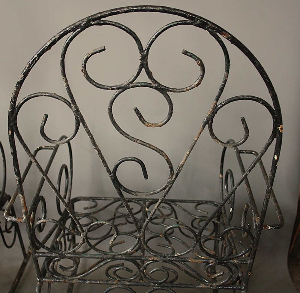 A pair of dark wrought iron garden rocking chairs featuring elaborate scrollwork patterns on the backrests, armrests, and bases. View IV