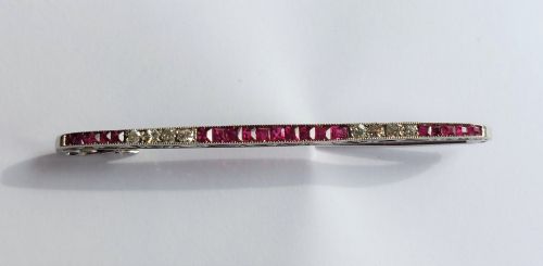fig 1. An Art Deco slender bar brooch crafted in white metal, channel-set with square red rubies interspersed with small round diamonds with millegrain detailing.