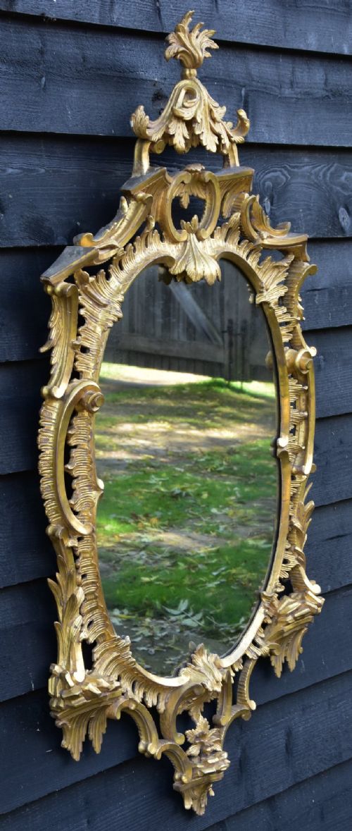 An 18th-century Georgian giltwood wall mirror featuring an oval mirror plate surrounded by an intricately carved gold leaf frame with acanthus leaf cresting and C-scroll motifs. View III
