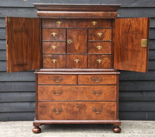 fig 2. A seventeenth-century William and Mary walnut cabinet on chest featuring double doors with decorative brass hinges above three drawers on bun feet.