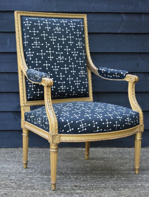 fig 1. A French Louis XVI style giltwood open armchair upholstered in dark blue fabric with white geometric motifs, featuring fluted legs and carved leaf moulding.