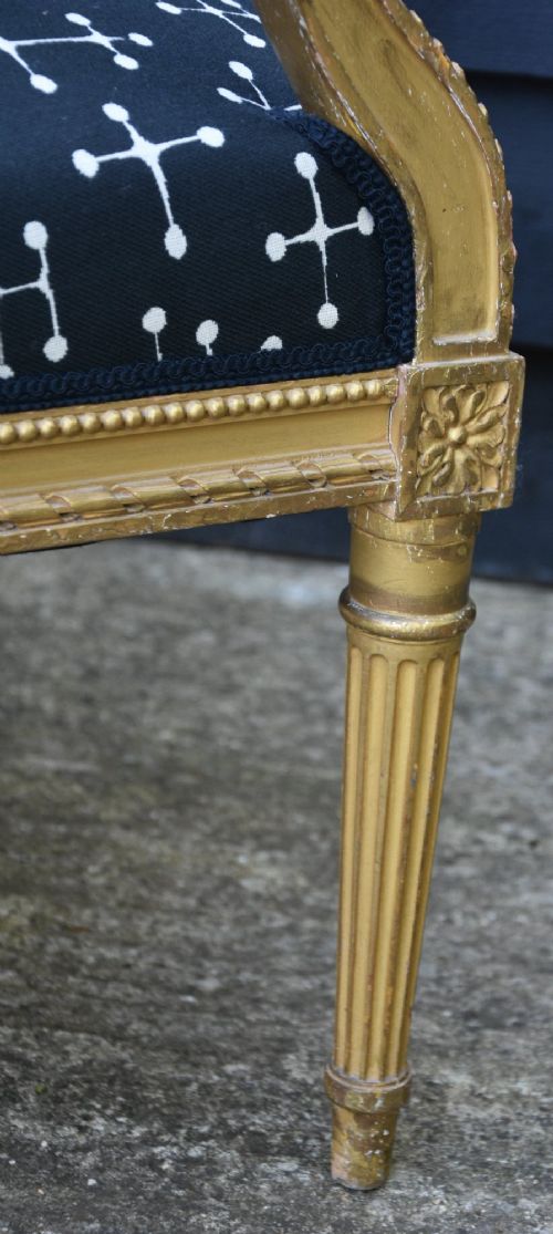 A French Louis XVI style giltwood open armchair upholstered in dark blue fabric with white geometric motifs, featuring fluted legs and carved leaf moulding. View VIII