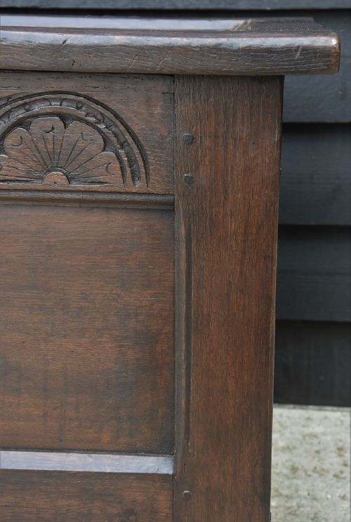 A dark 17th-century oak coffer featuring a carved lunette frieze, twin-panel front, hinged lid, and central iron escutcheon. View X