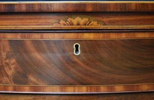 fig 1. A late 18th-century Georgian serpentine chest of drawers crafted from flame mahogany with satinwood crossbanding, four graduated drawers, brass knobs, and bracket feet.