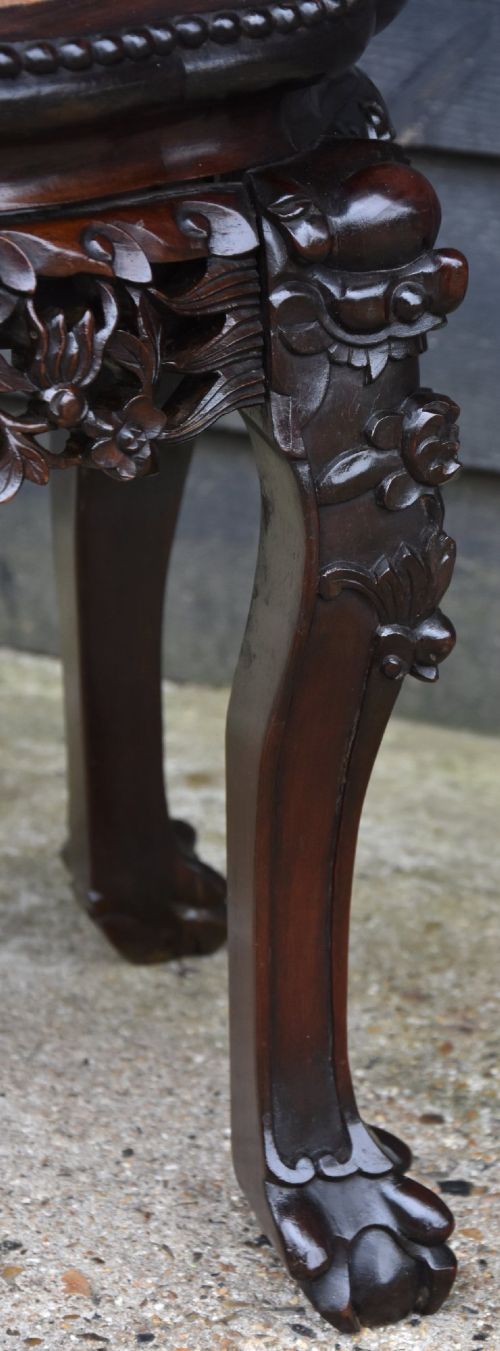 A 19th-century Chinese carved rosewood low plant stand featuring a circular marble insert top, an intricately pierced mask apron, cabriole legs, and claw feet. View V