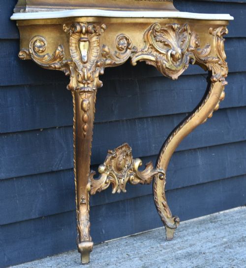 fig 2. A 19th-century French giltwood pier mirror with an ornate shell crest mounted above a matching carved console table featuring a marble top.