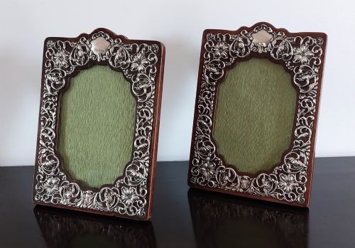 fig 1. A pair of ornate Edwardian silver photograph frames featuring detailed foliate repousse borders on dark wood backs with green textured centres.
