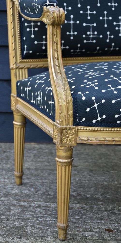 fig 1. A French Louis XVI style open armchair featuring a carved gold-leaf frame with fluted legs and dark navy fabric upholstery adorned with a white geometric pattern.