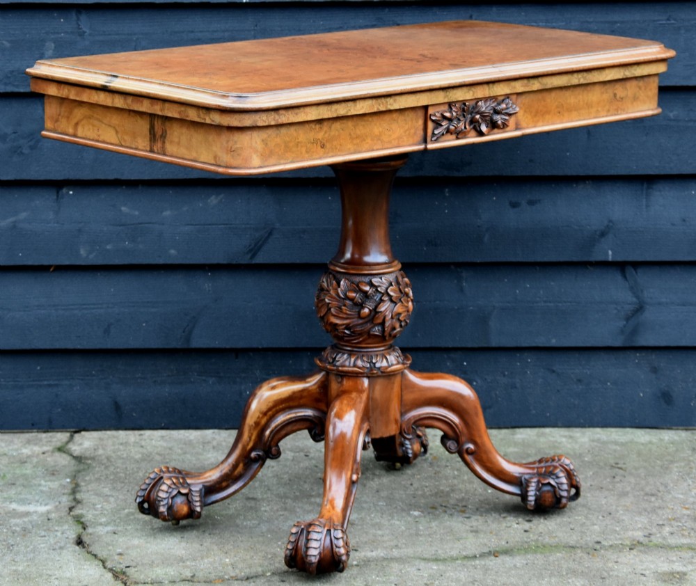 A Victorian burr walnut foldover card table featuring a rectangular swivel top, carved apron accent, turned pedestal stem with floral carving, and four cabriole legs ending in claw and ball feet. View II