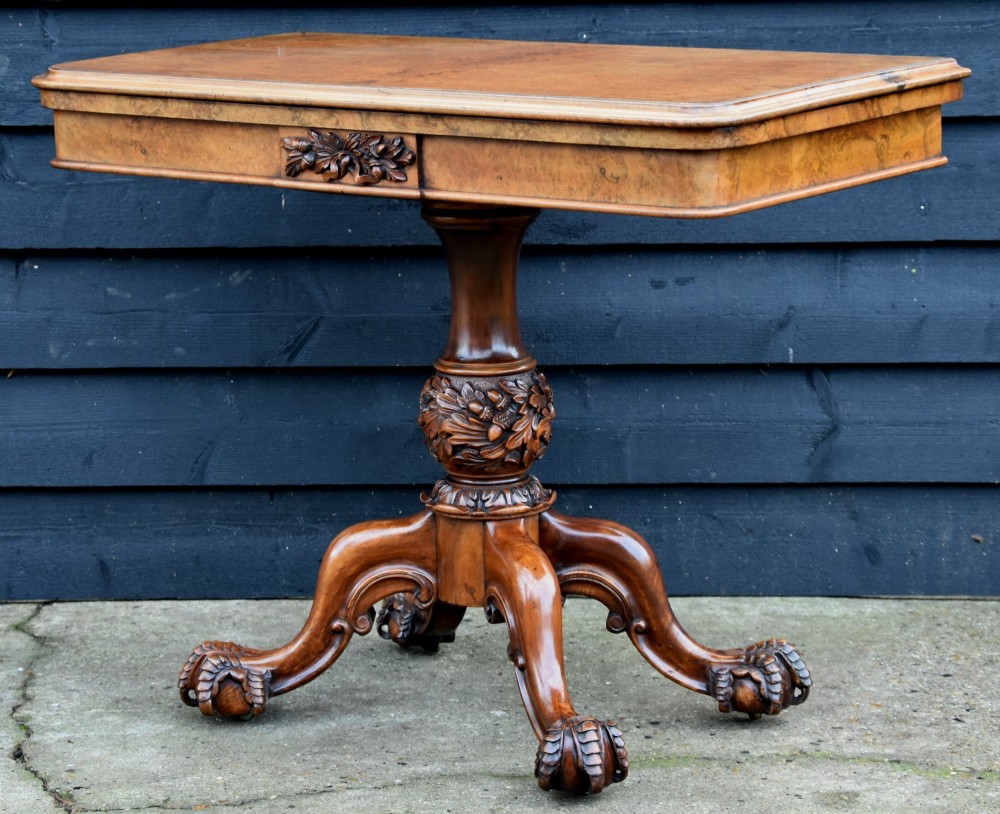 A Victorian burr walnut foldover card table featuring a rectangular swivel top, carved apron accent, turned pedestal stem with floral carving, and four cabriole legs ending in claw and ball feet. View III
