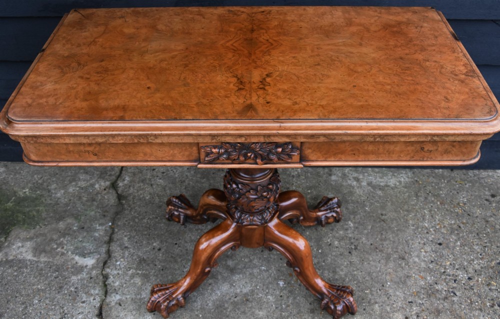 A Victorian burr walnut foldover card table featuring a rectangular swivel top, carved apron accent, turned pedestal stem with floral carving, and four cabriole legs ending in claw and ball feet. View VII