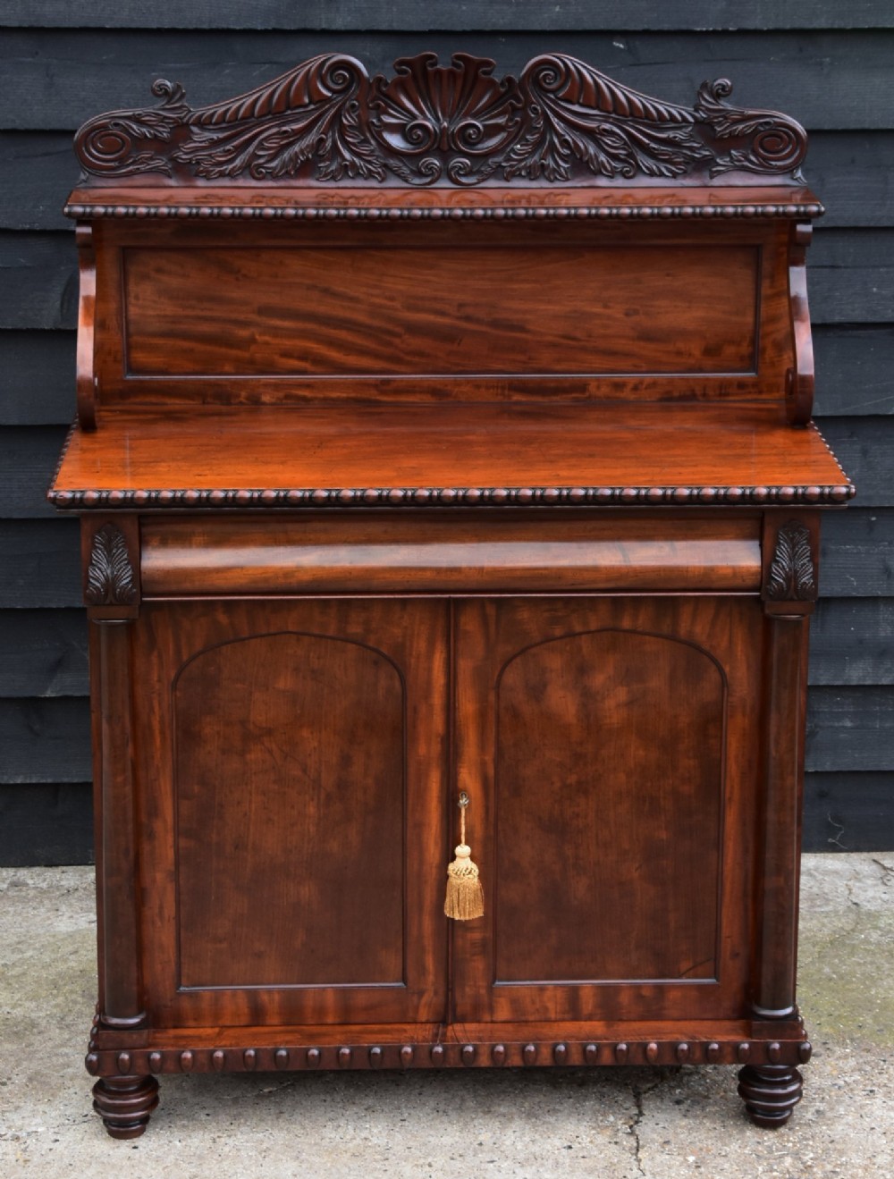 A Regency mahogany chiffonier side cabinet featuring a carved cresting gallery shelf, flame mahogany cupboard doors, and turned feet. View II