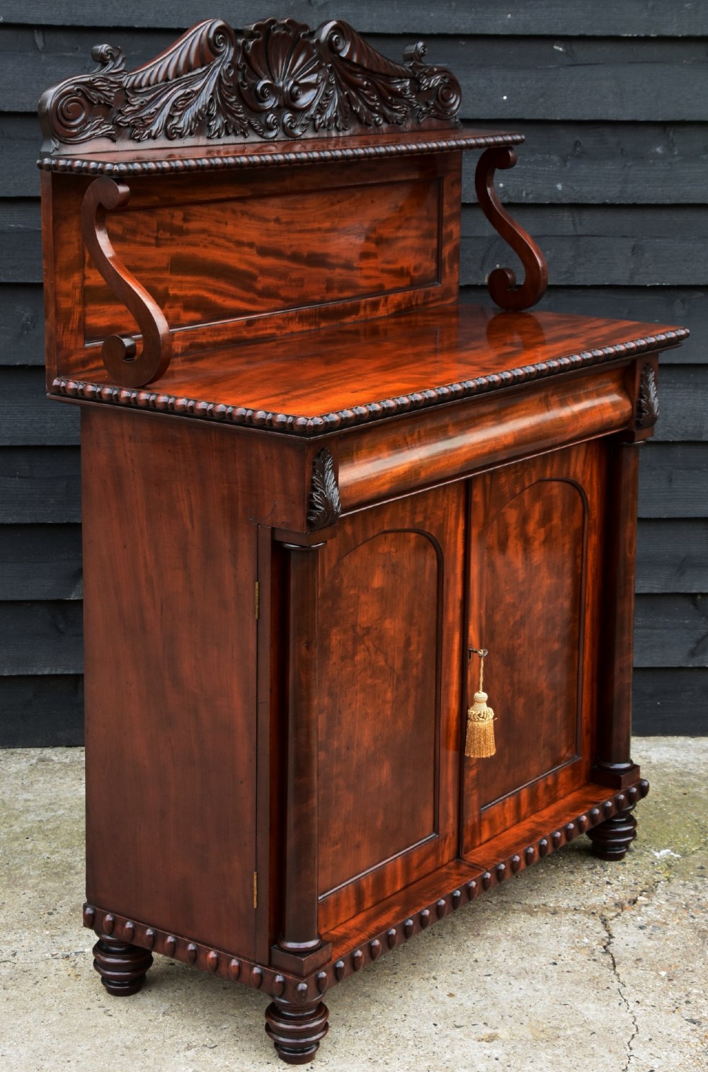 A Regency mahogany chiffonier side cabinet featuring a carved cresting gallery shelf, flame mahogany cupboard doors, and turned feet. View V