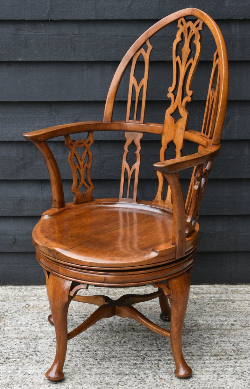 A late 19th-century Gothic Revival carved walnut revolving desk chair featuring an arched backrest with open tracery, curved armrests, a circular seat, and cabriole legs with an X-stretcher.