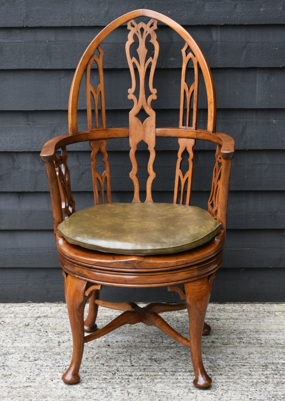 A late 19th-century Gothic Revival carved walnut revolving desk chair featuring an arched backrest with open tracery, curved armrests, a circular seat, and cabriole legs with an X-stretcher. View II