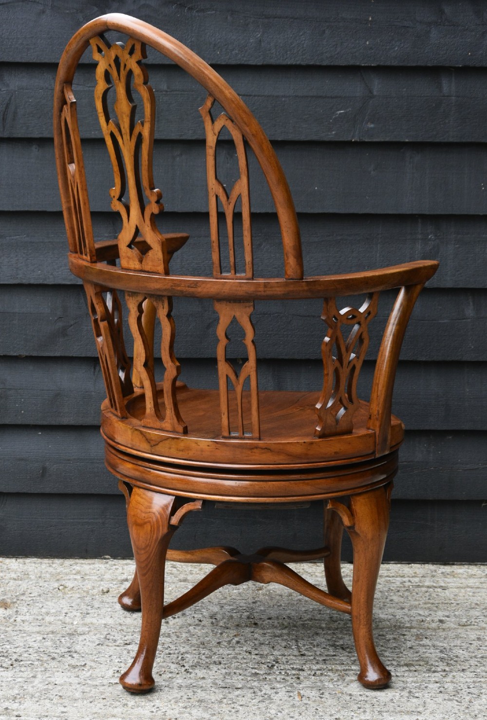 A late 19th-century Gothic Revival carved walnut revolving desk chair featuring an arched backrest with open tracery, curved armrests, a circular seat, and cabriole legs with an X-stretcher. View V