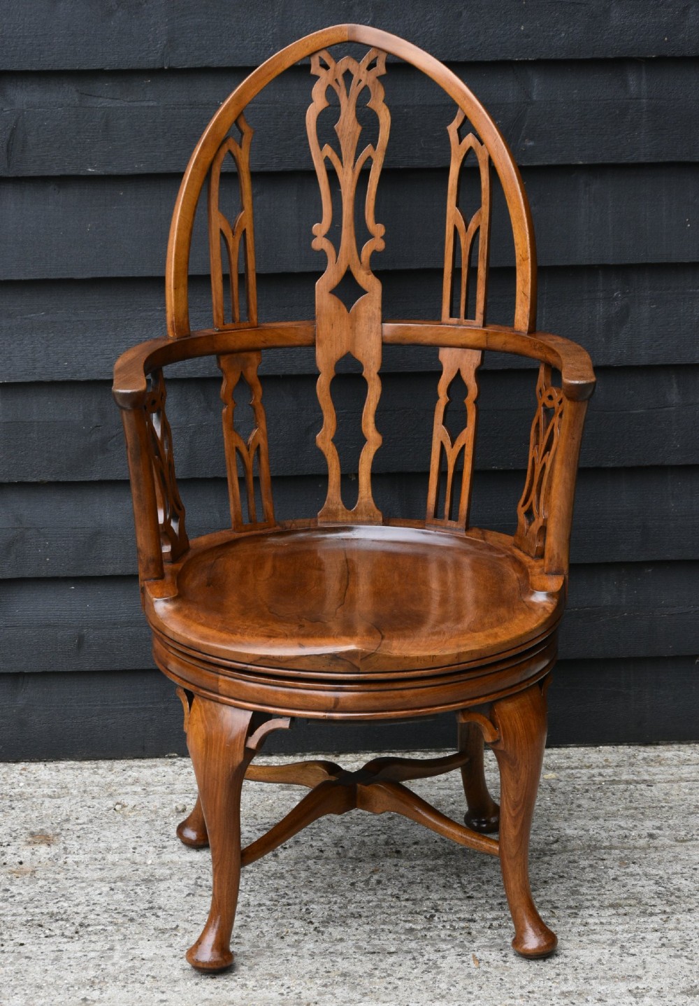 A late 19th-century Gothic Revival carved walnut revolving desk chair featuring an arched backrest with open tracery, curved armrests, a circular seat, and cabriole legs with an X-stretcher. View VII