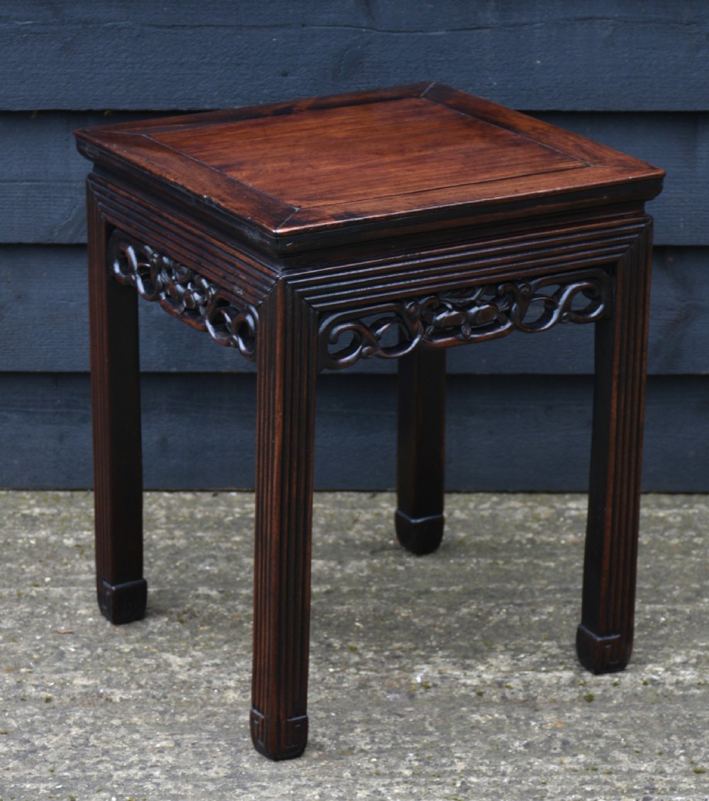 A dark rosewood square low table featuring a framed panel top, openwork carved aprons, and reeded legs.