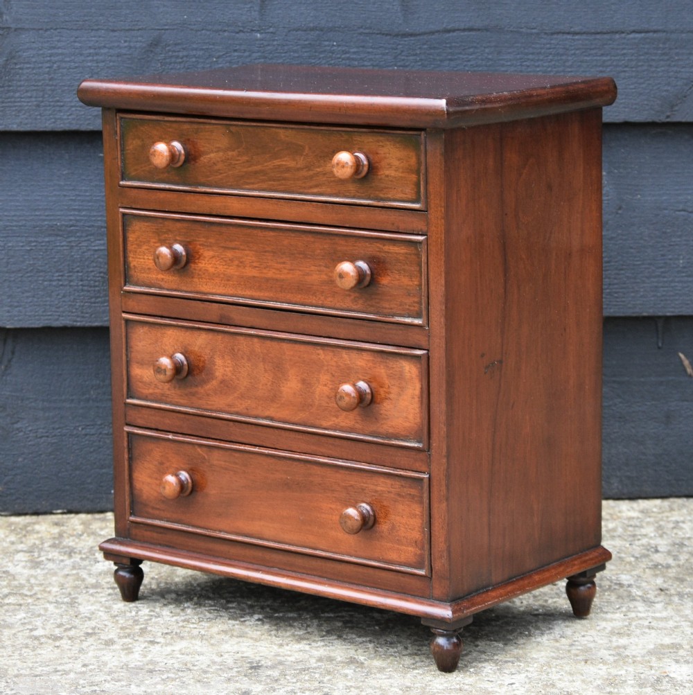A Victorian mahogany miniature chest of drawers with four graduated drawers, turned wooden knobs, and turned feet.