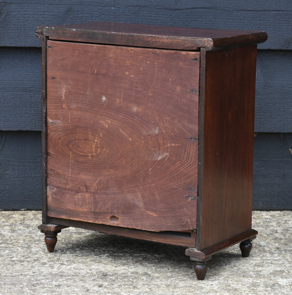A Victorian mahogany miniature chest of drawers with four graduated drawers, turned wooden knobs, and turned feet. View IV