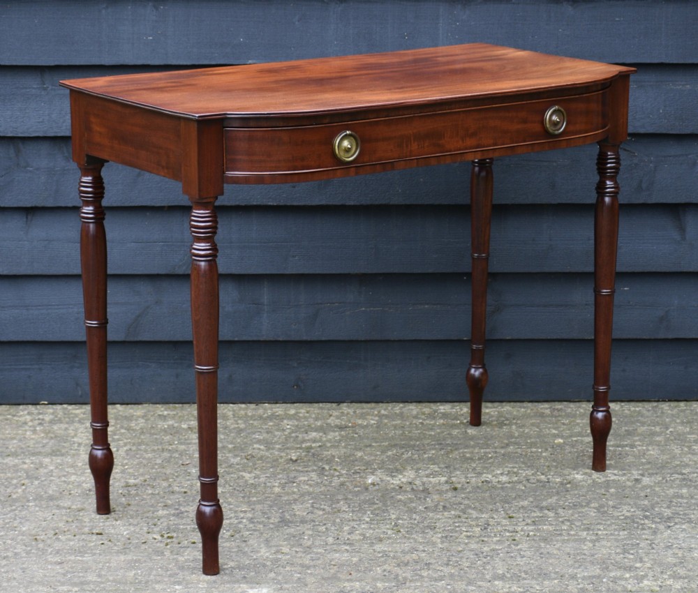 A Regency mahogany bow-fronted side table featuring a central drawer with circular brass handles and slender turned legs.