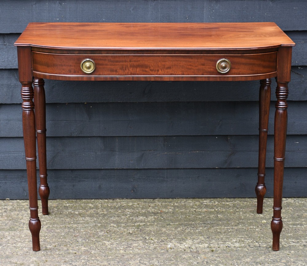 A Regency mahogany bow-fronted side table featuring a central drawer with circular brass handles and slender turned legs. View II