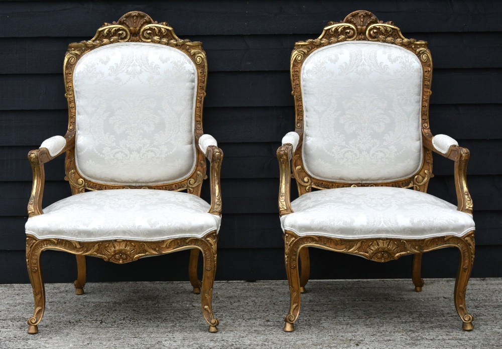 Pair of late 19th-century French giltwood armchairs upholstered in cream damask with carved cresting and cabriole legs.