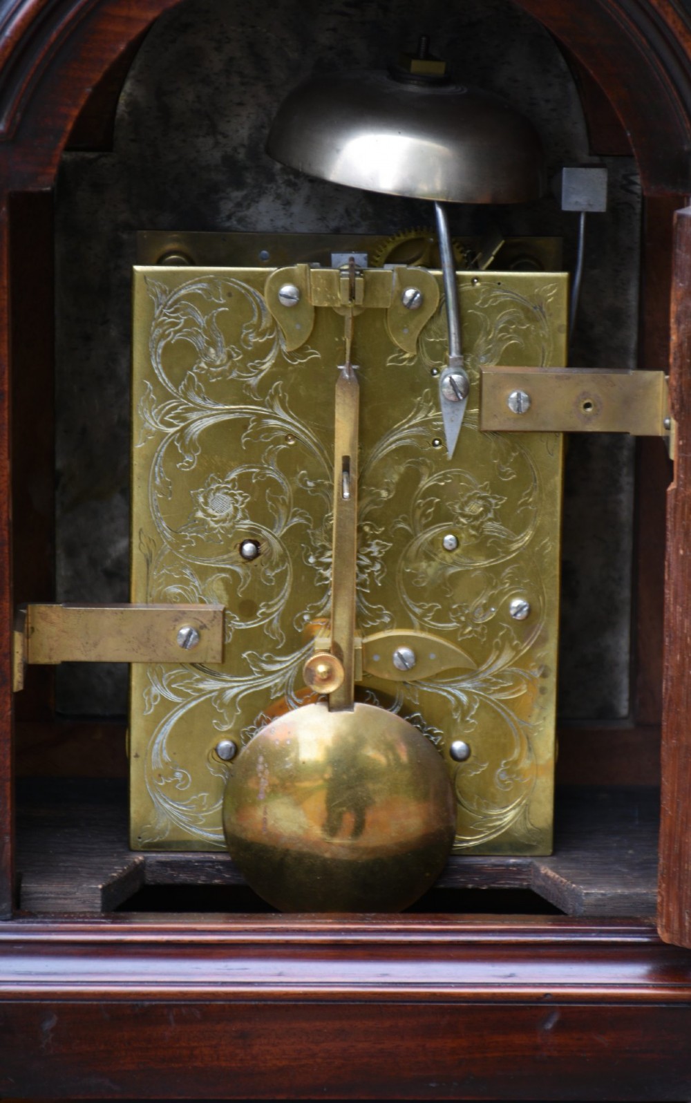 A Georgian mahogany bracket clock featuring an arched top case, top brass carrying handle, pierced side fretwork, engraved dial with Roman numerals, and brass bracket feet. View VII