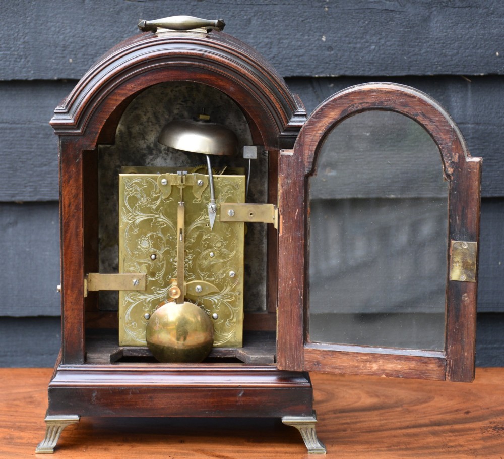 A Georgian mahogany bracket clock featuring an arched top case, top brass carrying handle, pierced side fretwork, engraved dial with Roman numerals, and brass bracket feet. View VIII