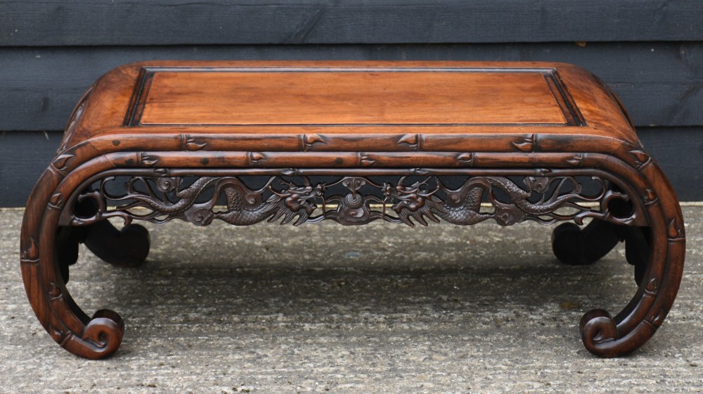 A low Chinese rosewood table with relief-carved dragon aprons, simulated bamboo moulding, and inward-curving scroll feet.