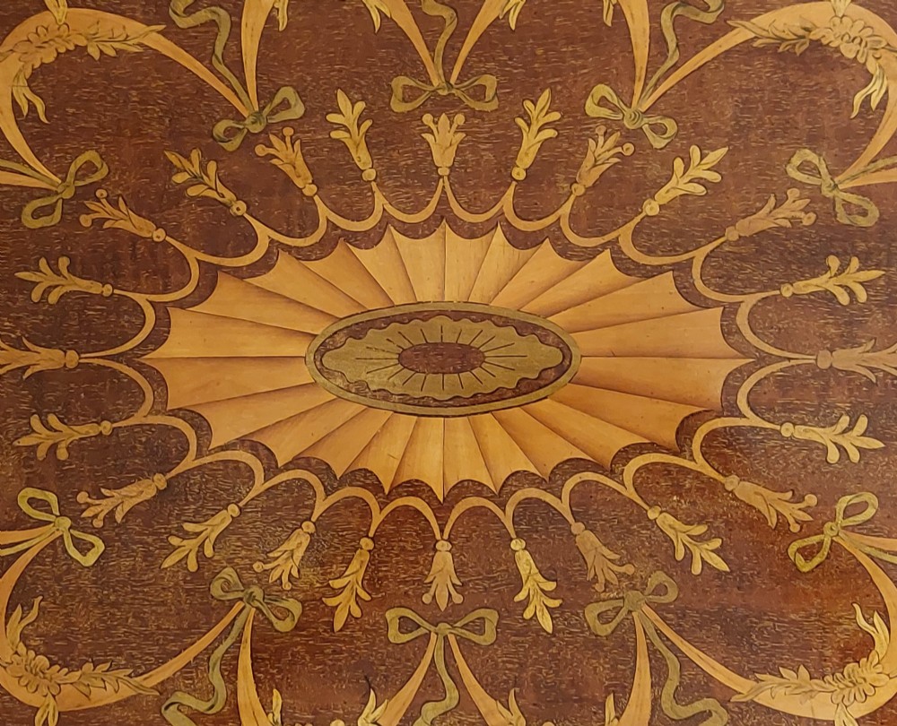 An oval mahogany serving tray featuring intricate central floral marquetry inlay, ribbon swags, and two cast brass side handles. View IV