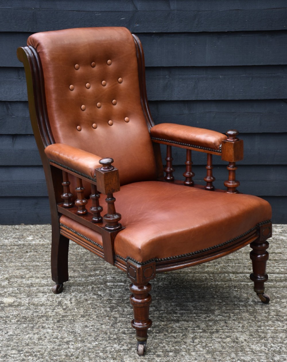 A 19th-century mahogany library armchair upholstered in buttoned brown leather with turned spindle arm supports and brass castors.