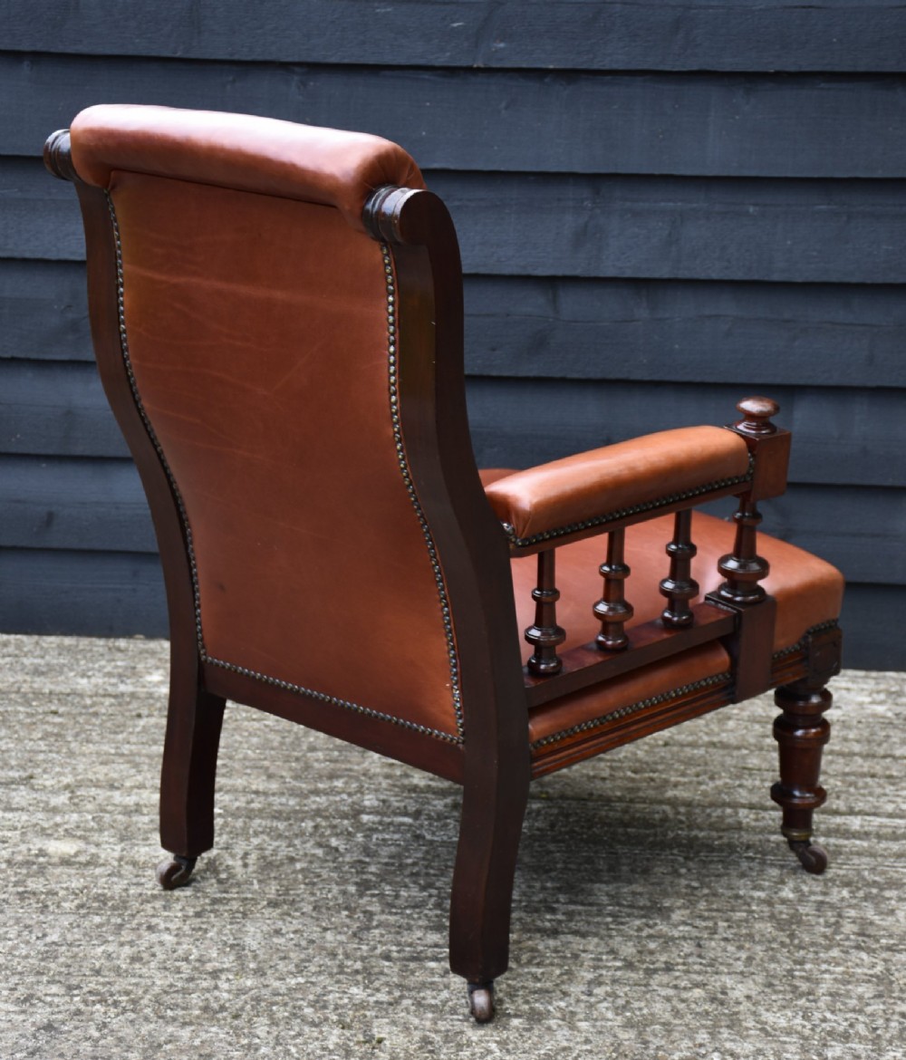 A 19th-century mahogany library armchair upholstered in buttoned brown leather with turned spindle arm supports and brass castors. View II